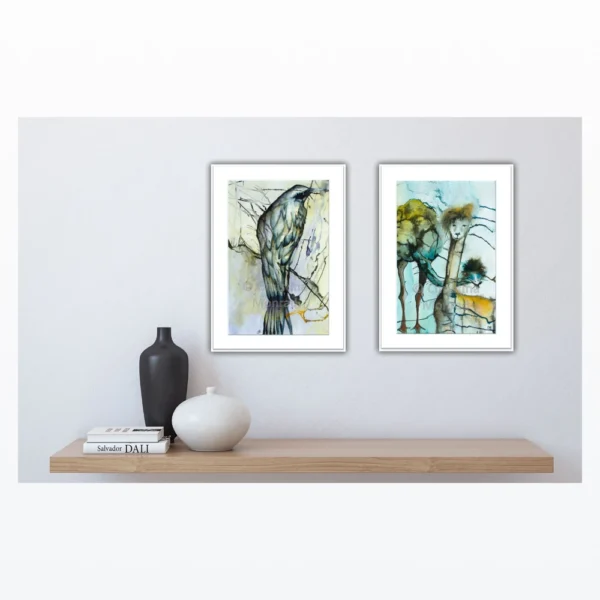 To kunstværker hænger over hylde: én med fugl på gren og én med abstrakte giraffer og træer i baggrunden.