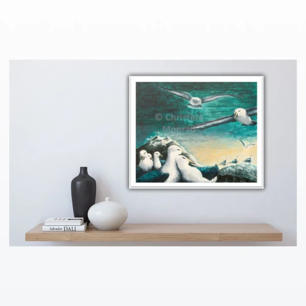 Maleri af havfugle på klippe og i flugt over havet i dæmpede blå og grønne farver hænger over træhylde.